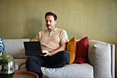 Mann mit Laptop auf Sofa im Wohnzimmer