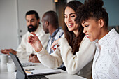 Smiling women sitting at business meeting and looking at laptop\n