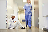 Female doctor sitting on hospital corridor floor\n