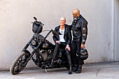 Cool mature biker couple in leather clothes posing with motorcycle\n