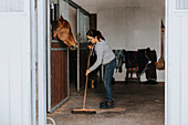 Woman in stable sweeping floor\n