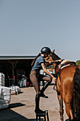 Seitenansicht einer Frau beim Aufsteigen auf ein Pferd auf der Koppel