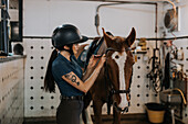 Woman in stable preparing horse for horse riding\n