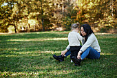 Mother and daughter sitting with daughter in autumn park\n