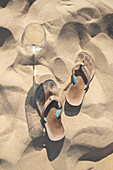 Wine glass and flip-flops on sandy beach\n