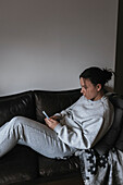 Junge Frau sitzt auf dem Sofa und benutzt ein Handy
