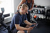 Mann und Frau schauen auf ein digitales Tablet im Fitnessstudio