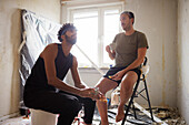 Smiling male homosexual couple having coffee break during apartment renovation\n