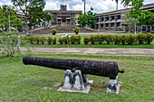 Eine Kanone aus der Kolonialzeit auf dem Independence Plaza in der Hauptstadt Belmopan, Belize. Dahinter befindet sich das Gebäude der Nationalversammlung.