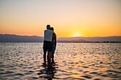 Umarmendes Paar genießt den Sonnenuntergang am Strand von Trabucador, Ebro-Delta, Tarragona, Spanien