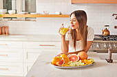 Woman drinking fresh citrus juice in kitchen\n
