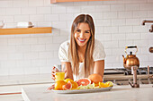 Portrait of smiling woman with glass of fresh citrus juice in kitchen\n