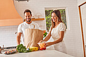 Smiling couple with paper shopping bag and groceries in kitchen\n