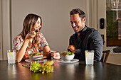 Smiling couple enjoying salad at table at home\n
