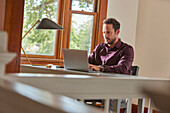 Man using laptop at table at home\n