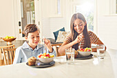 Smiling boy (8-9) and girl (12-13) having breakfast in kitchen\n