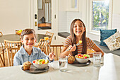 Smiling boy (8-9) and girl (12-13) enjoying breakfast in kitchen\n