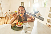 Smiling girl (12-13) having breakfast in kitchen\n
