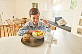 Smiling boy (8-9) enjoying breakfast in kitchen\n