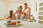 Smiling family with two children (8-9, 12-13) eating fresh fruit in kitchen\n