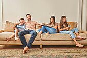 Lächelnde Familie mit zwei Kindern (8-9, 12-13) entspannt auf dem Sofa