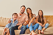 Portrait of smiling family with two children (8-9, 12-13) watching TV on sofa\n