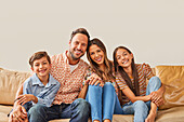 Portrait einer lächelnden Familie mit zwei Kindern (8-9, 12-13) auf dem Sofa sitzend
