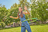 Smiling girl (12-13) playing with hula hoop in park\n