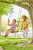 Smiling mother with and son (8-9) on swing in park\n