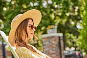 Woman in straw hat and sunglasses relaxing in park\n
