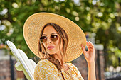 Woman in straw hat and sunglasses relaxing in park\n