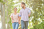 Smiling couple holding hands, walking on treelined sidewalk\n