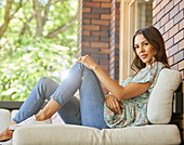 Porträt einer Frau mittleren Alters, die sich auf dem Sofa auf der Terrasse entspannt