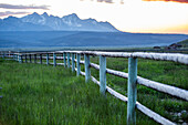 USA, Idaho, Stanley, Scenic view of Sawtooth Mountains and meadow with rail fence at sunset\n