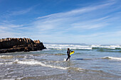 Südafrika, Hermanus, Junge (10-11) betritt Atlantik mit Bodyboard in Kammabaai Beach