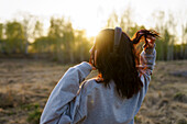 Rückansicht einer musikhörenden Frau auf einer Wiese bei Sonnenuntergang