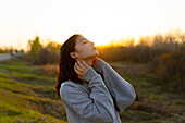 Portrait einer nachdenklichen Frau mit geschlossenen Augen auf einer Wiese bei Sonnenuntergang