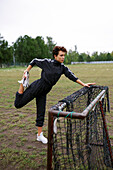 Young woman stretching legs while leaning on mini soccer goal \n