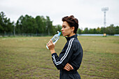 Young woman drinking water after sports training\n
