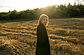 Porträt einer jungen Frau, die bei Sonnenuntergang in einem Feld steht