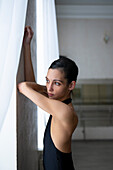 Ballerina leaning on wall and looking through window \n