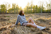 Brunette woman sitting in meadow and listening to music \n