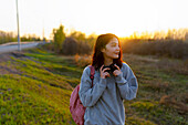 Woman with headphones and backpack, looking away at sunset \n