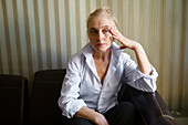 Serious blonde woman sitting on sofa in living room \n