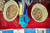 Hochformatige Ansicht eines Arbeiters, der sich neben Strohkörben voller Samen für die Herstellung von Arganöl ausruht, Marokko, Nordafrika, Afrika