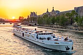 Frankreich, Paris, von der UNESCO zum Weltkulturerbe erklärtes Gebiet, ein festliches Kreuzfahrtschiff fährt bei Sonnenuntergang am Louvre vorbei