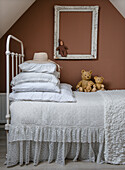 Single bed with lace blanket, pillows and teddy bears, empty picture frame on the wall