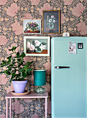 Retro-Kühlschrank und Pflanze vor floraler Tapete und Blumenbildern