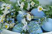 Schale gefüllt mit Ostereiern, Gänseblümchen und Vergissmeinnicht