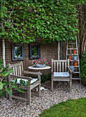 Cozy seating area with wooden table and chairs in the garden in front of brick wall